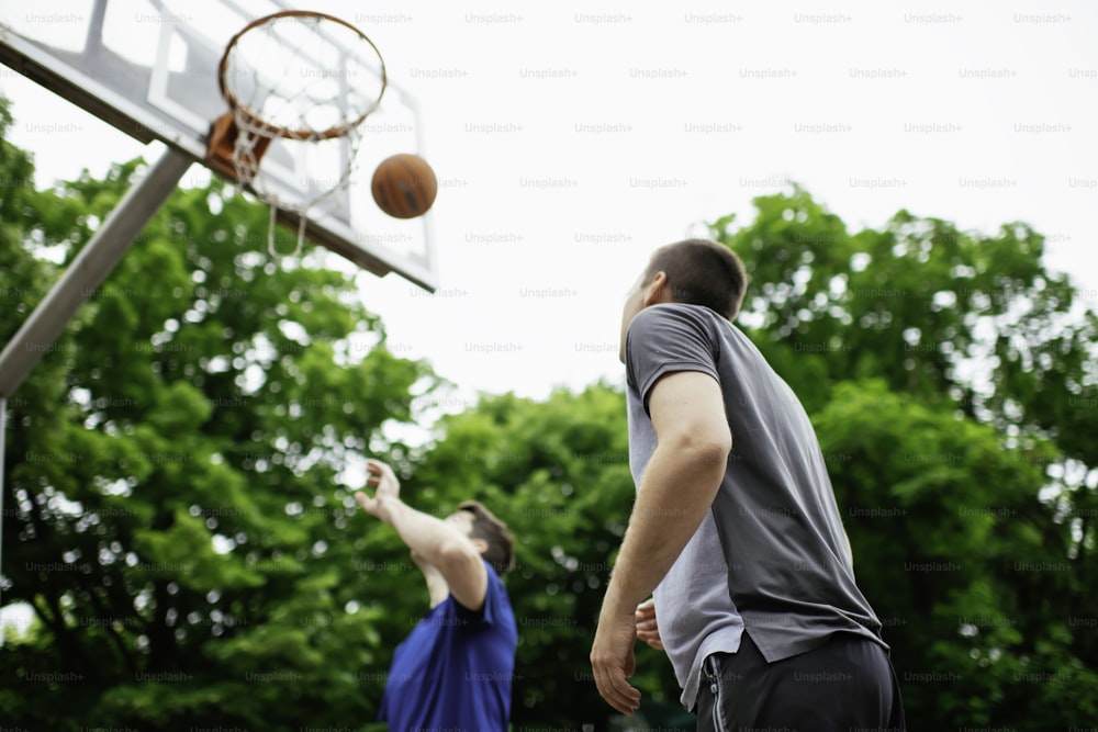 公園でバスケットボールをする2人の青年。屋外で親善試合を行う友人たち
