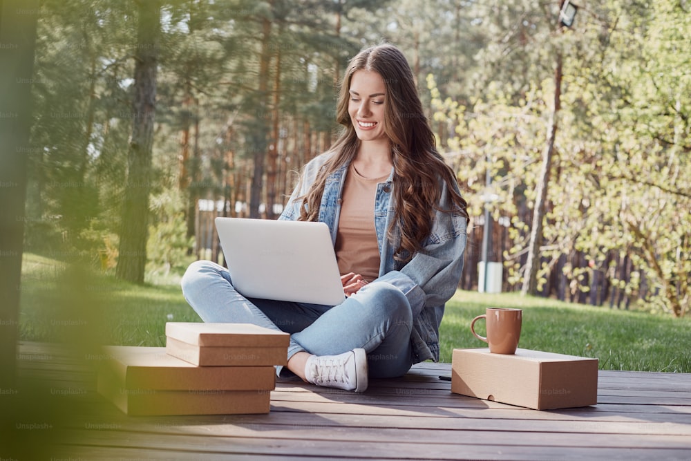 Charming woman being concentrated on work while using a laptop and sitting on terrace in forest