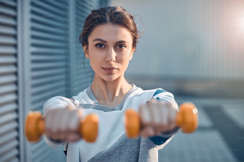 Sportswoman holding a pair of dumbbells in her outstretched arms in front of the camera