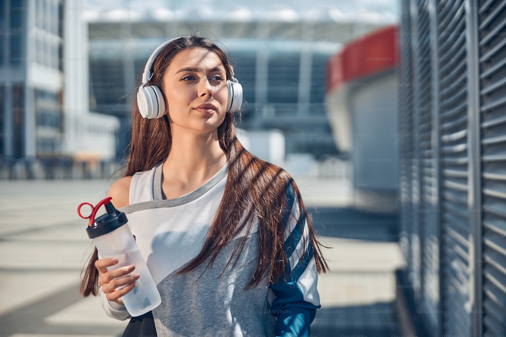Waist-up portrait of a beautiful pensive Caucasian sportswoman in wireless headphones staring into the distance