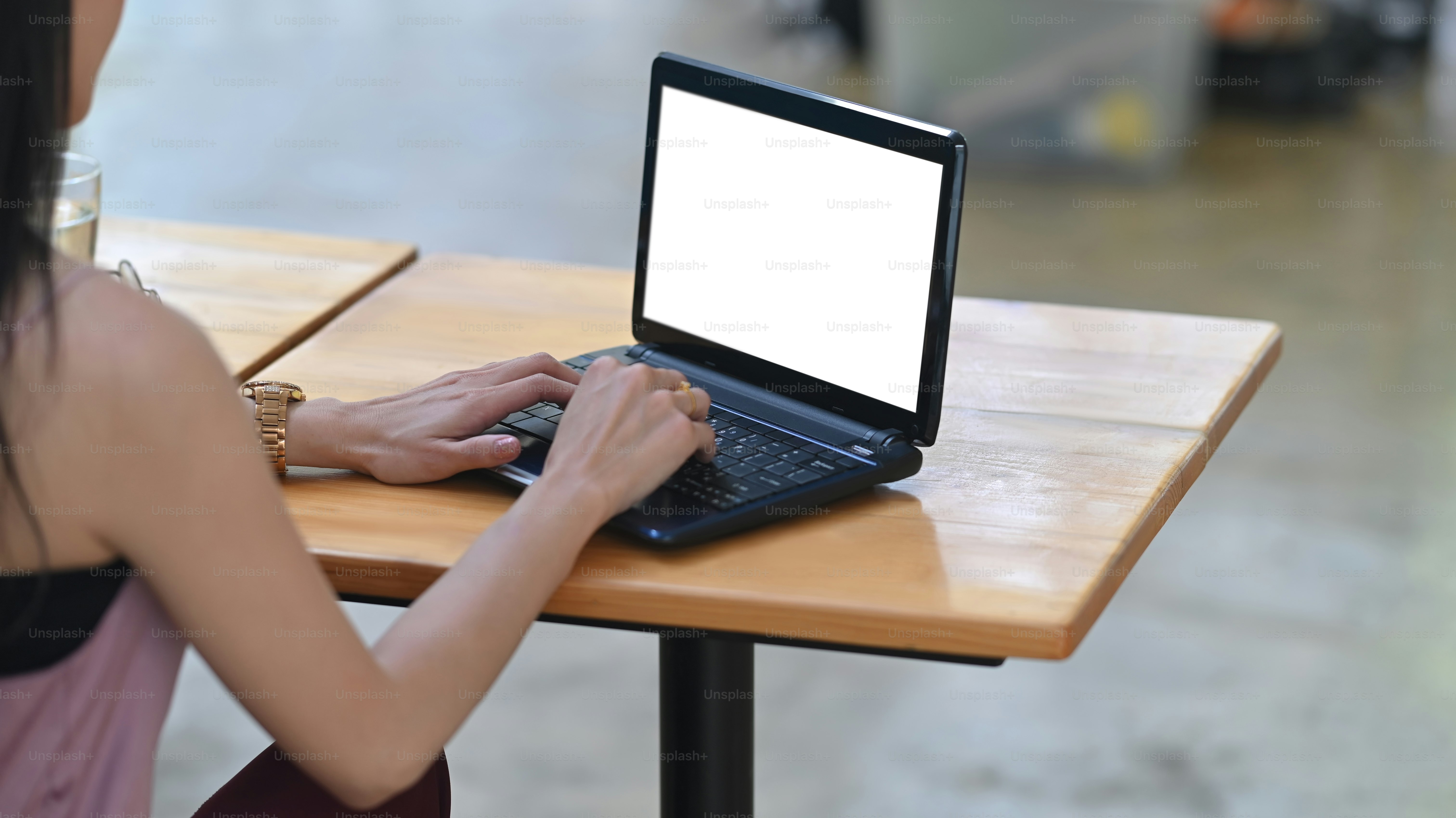 Behind shot of beautiful woman is working with a white blank screen computer laptop at the wooden desk.