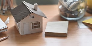 Um modelo de casa está colocando em uma mesa de trabalho de madeira cercada por economizar dinheiro e equipamentos pessoais.