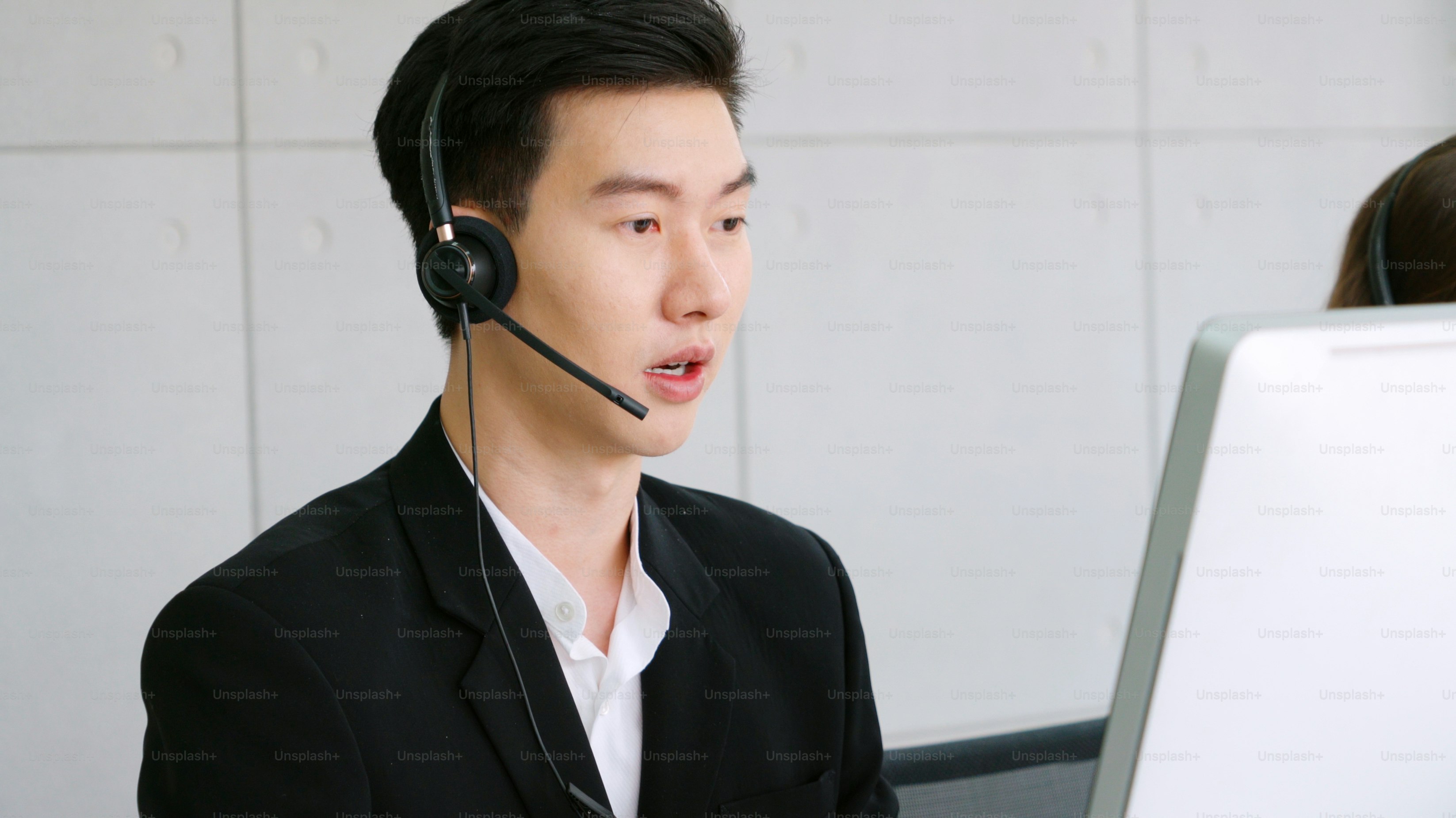 A man in a black suit wearing a headset at a computer workstation