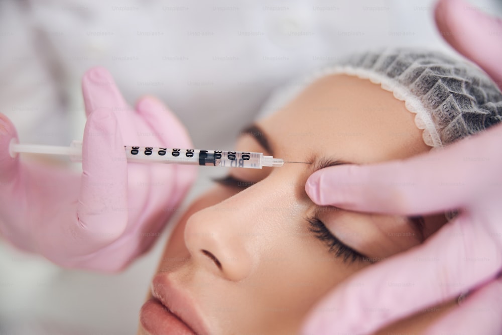Pleasant calm woman keeping eyes closed while receiving eyebrow injection by qualified beautician