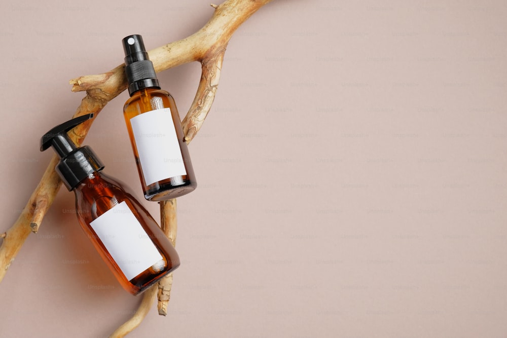 Cosmetics SPA branding mockup. Dark amber glass bottles with white labels for text on wood branch. Pump dispenser bottle for cosmetic and body spray bottle. Flat lay, top view.