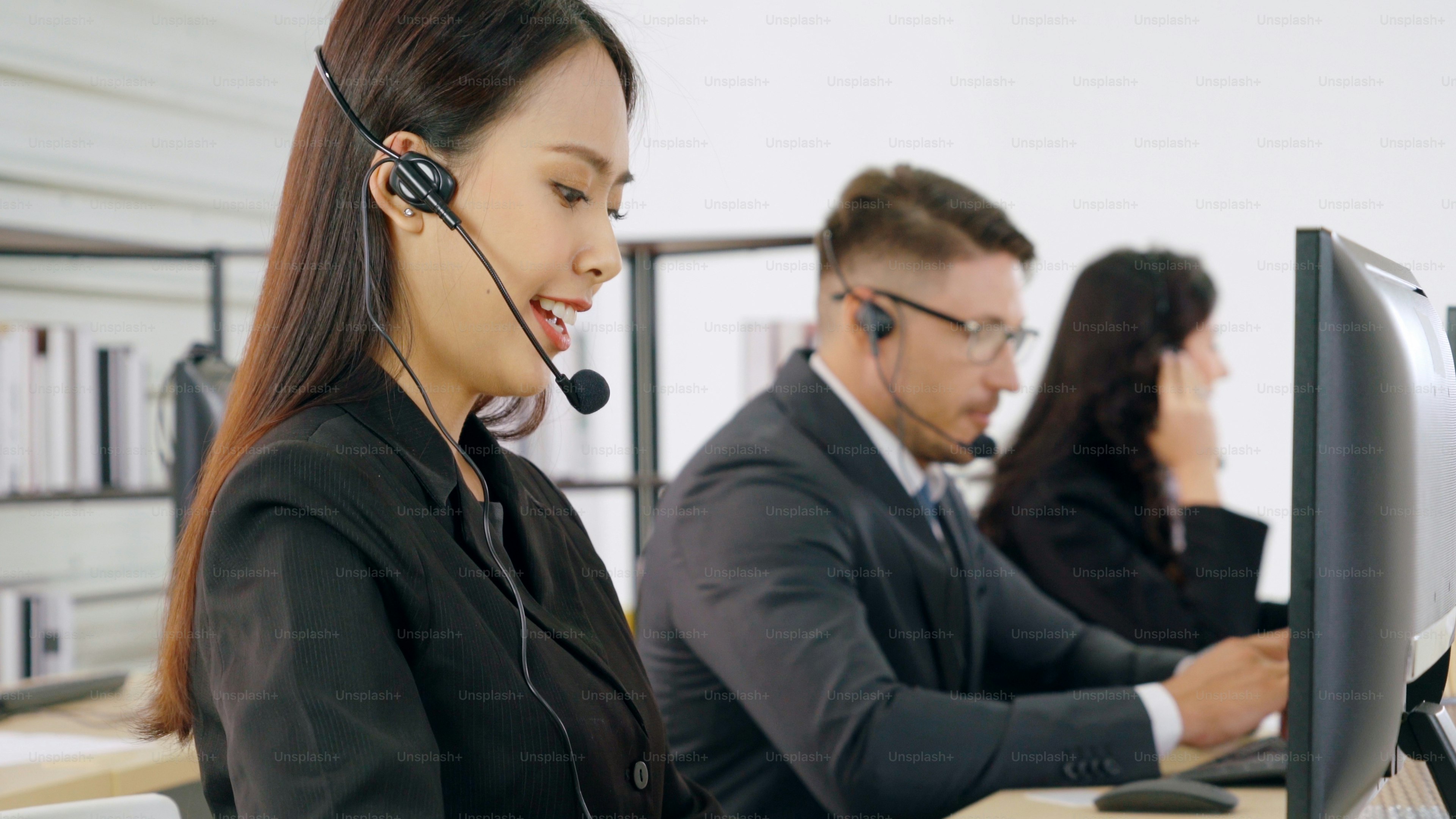 Three customer service representatives wearing headsets while working at computers in an office