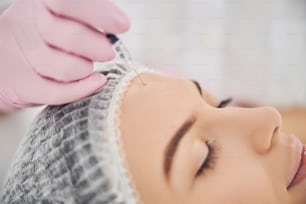 Restful woman getting beauty injection in forehead while keeping her eyes closed