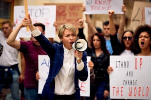 Caucasian woman with megaphone shouting while standing in front of crowd of people on a protest for human rights.