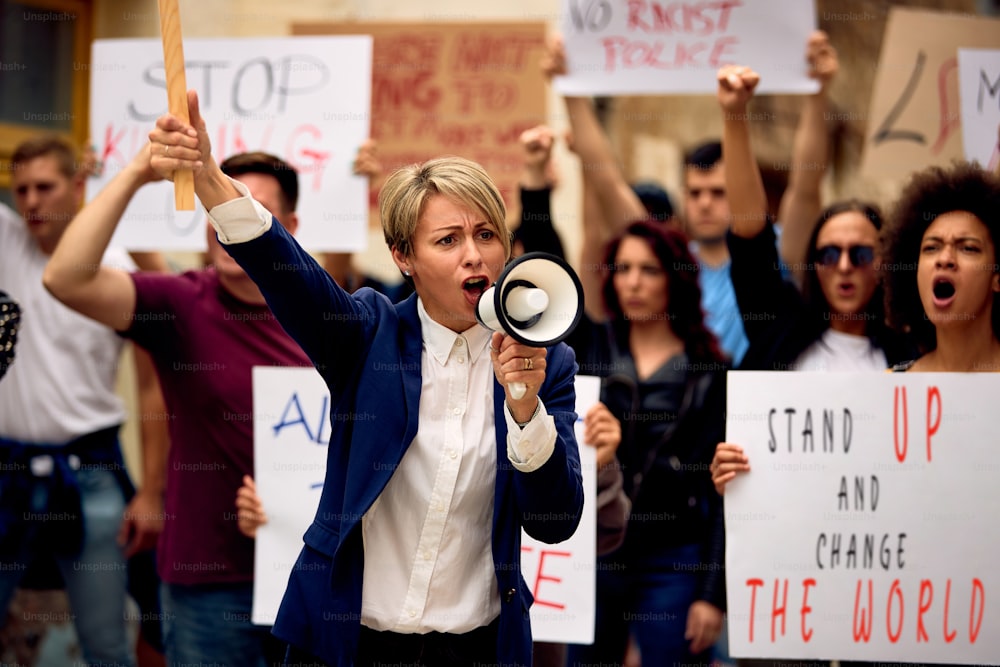 Mulher caucasiana com megafone gritando enquanto estava na frente de uma multidão de pessoas em um protesto pelos direitos humanos.