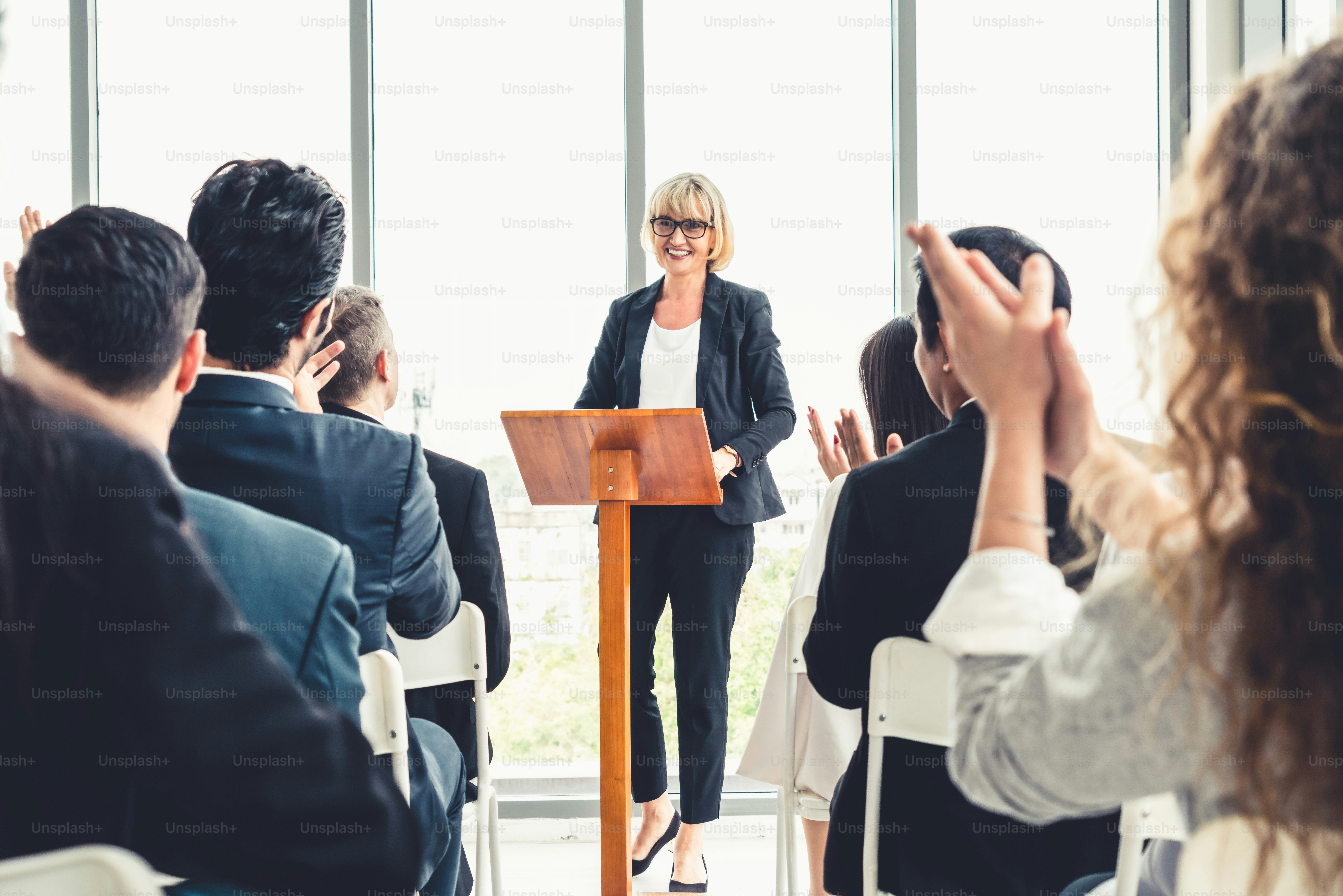 Group of business people meeting in a seminar conference . Audience listening to instructor in employee education training session . Office worker community summit forum with expert speaker .