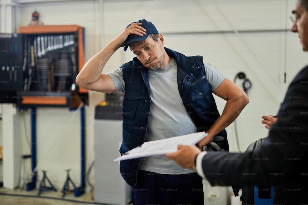 Distraught car mechanic going through problematic paperwork with his manager in auto repair shop.