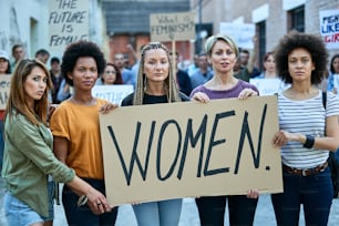 Group of females holding a banner with inscription 'women' while participating in street demonstrations.