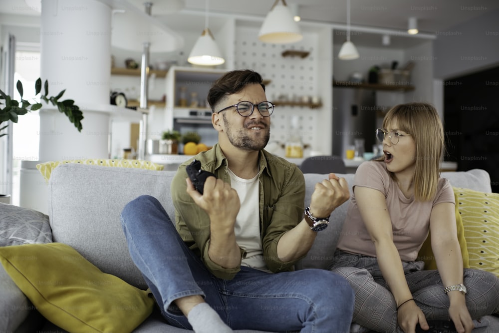 Boyfriend and girlfriend playing video game with joysticks in living room.
Loving couple are playing video games at home.