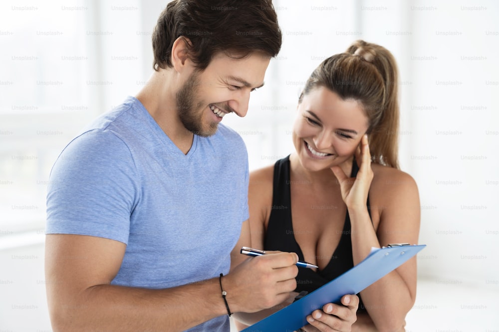 Man and woman are ready for workout in the gym. Personal fitness instructor writing individual training and diet plan for his client
