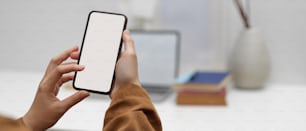 Close up view of female worker using mock-up smartphone in office room with laptop and supplies in blurred background