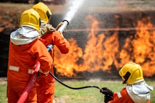 Un groupe de pompiers travaille en équipe à l’aide d’eau et de mousse chimique pulvérisant des flammes d’incendie dans des locaux en feu.