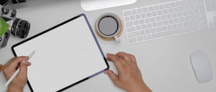 Foto aérea de mãos masculinas usando o tablet de maquete na mesa de trabalho branca com dispositivo de computador