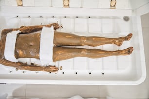 Top view of an unrecognizable Caucasian woman lying in a comfortable spa capsule with body mask on her skin