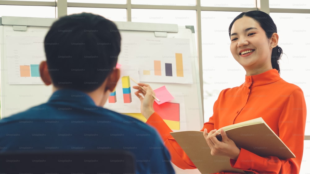 Young woman explains business data on white board in casual office room . The confident Asian businesswoman reports information progress of a business project to partner to determine market strategy .