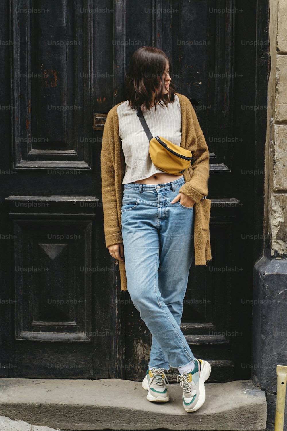 Stylish hipster girl standing at building in european city street. Young woman in casual fashionable outfit posing at old wooden door. Alone leisure activity in city