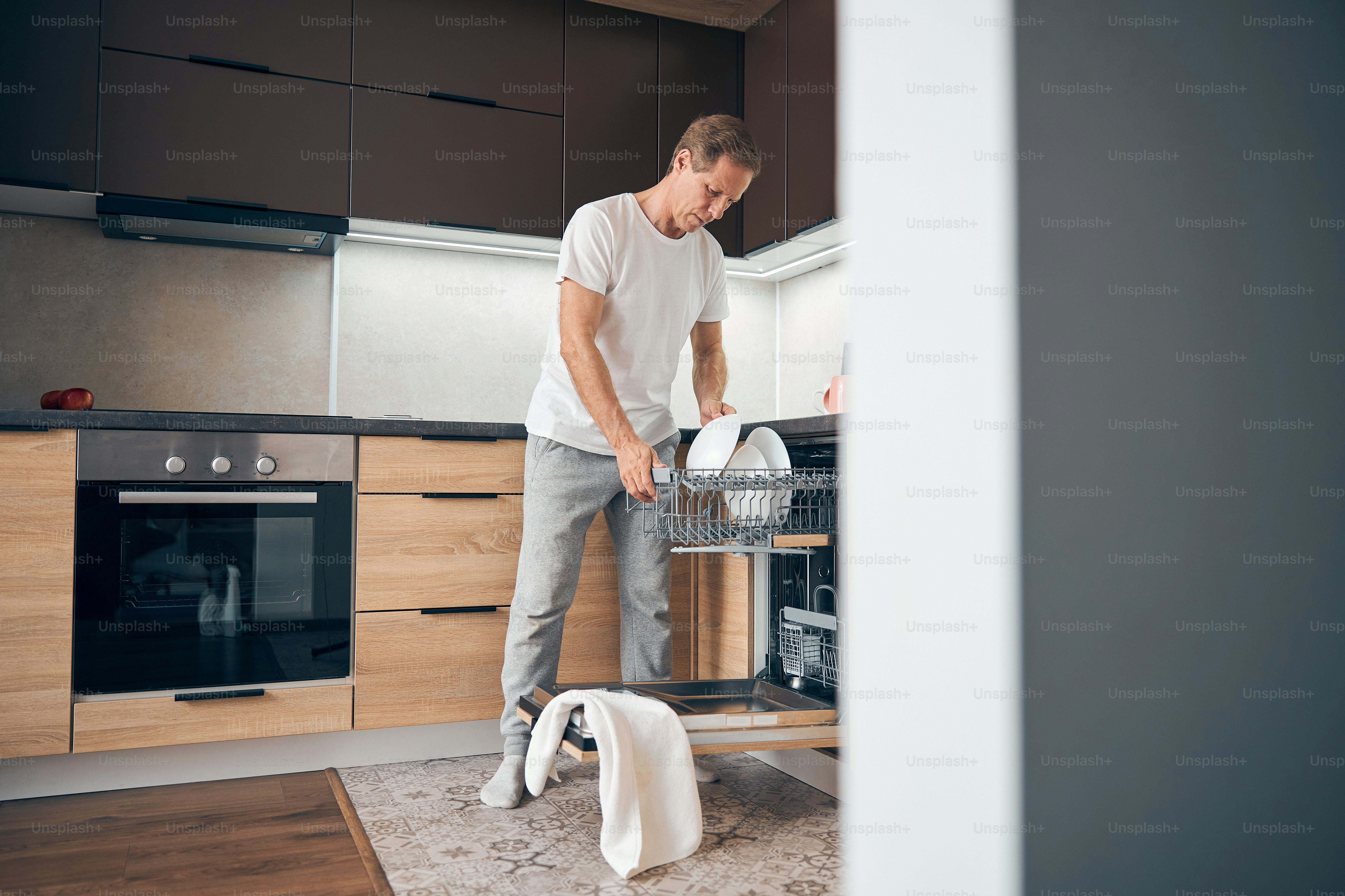 Happy adult male person being in the kitchen and cleaning up after having dinner