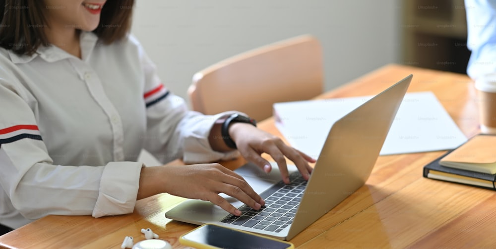 Una giovane segretaria sta digitando su un computer portatile mentre è seduta alla scrivania di legno.