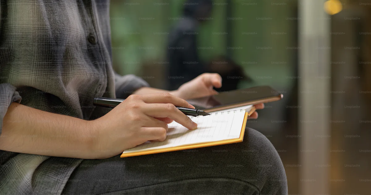 Side view of female worker sitting on worktable and taking note on ...