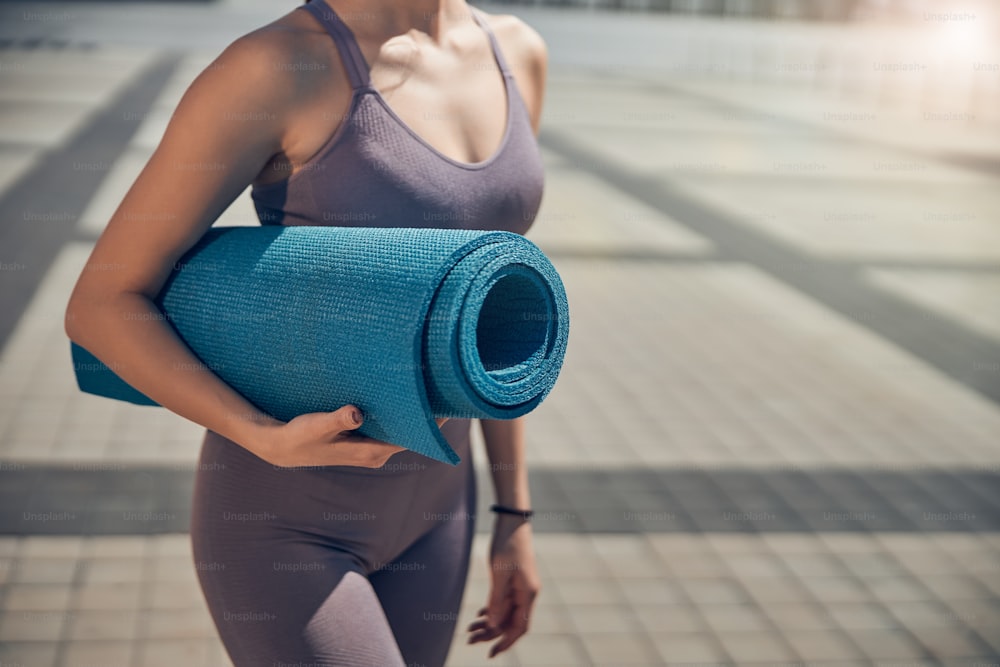 Cropped photo of an athletic young lady holding a rolled-up yoga mat under her arm