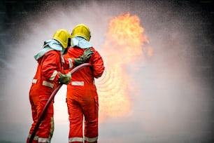 Zwei Feuerwehrleute arbeiten im Feuerwehranzug mit Feuerlöschausrüstung unter Verwendung von Hochdruckwasser ein Feuer bekämpfen