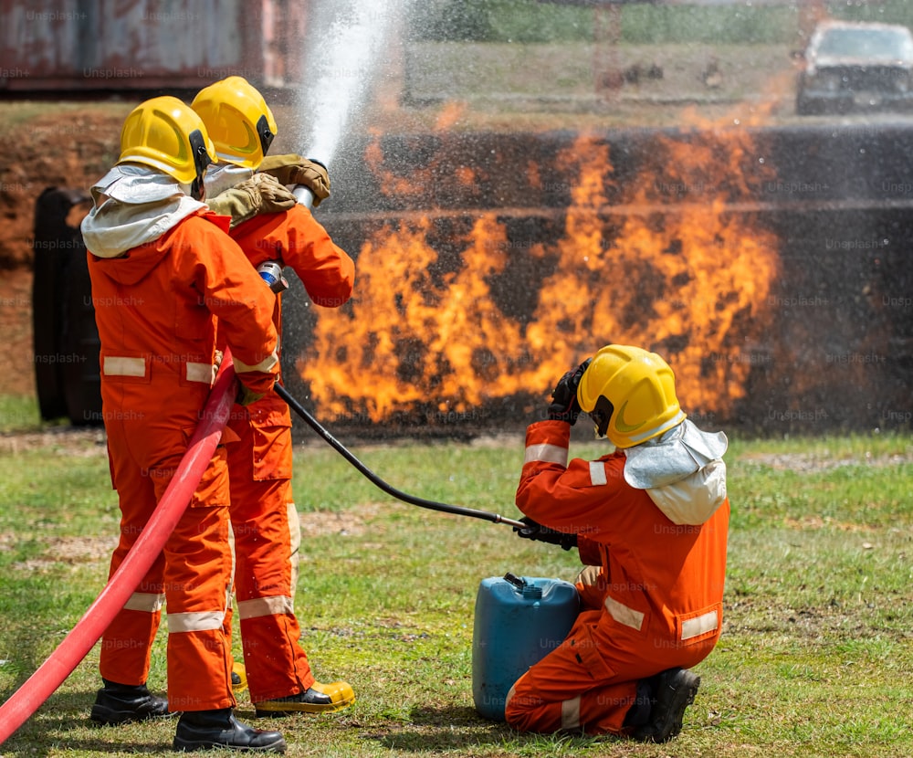 Grupo de bombeiros em equipe utilizando água e espuma química pulverizando chamas de incêndio em instalações em chamas.