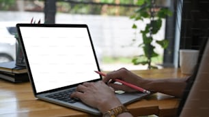 Cropped image of a woman's hand is working with a white blank screen computer laptop at the wooden desk.