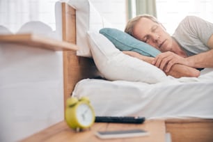 Kind adult male person keeping eyes closed while having rest after working day in his bedroom