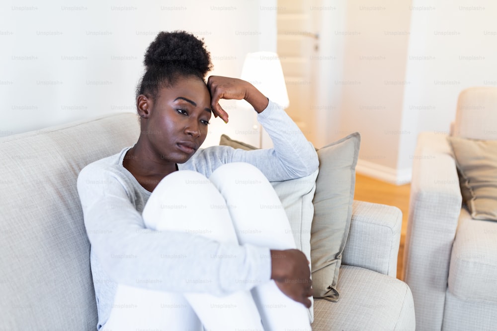 悲しい思慮深い心配なアフリカ系アメリカ人の女の子はソファに座って目をそらし、落ち込んで疑いを感じ、孤独でストレスを感じ、心理的な問題を考えている動揺した若い黒人の女の子が間違いについて後悔している
