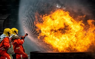 Two Firefighter teamwork in fire suit with fire fighting equipment using high pressure water fight a fire