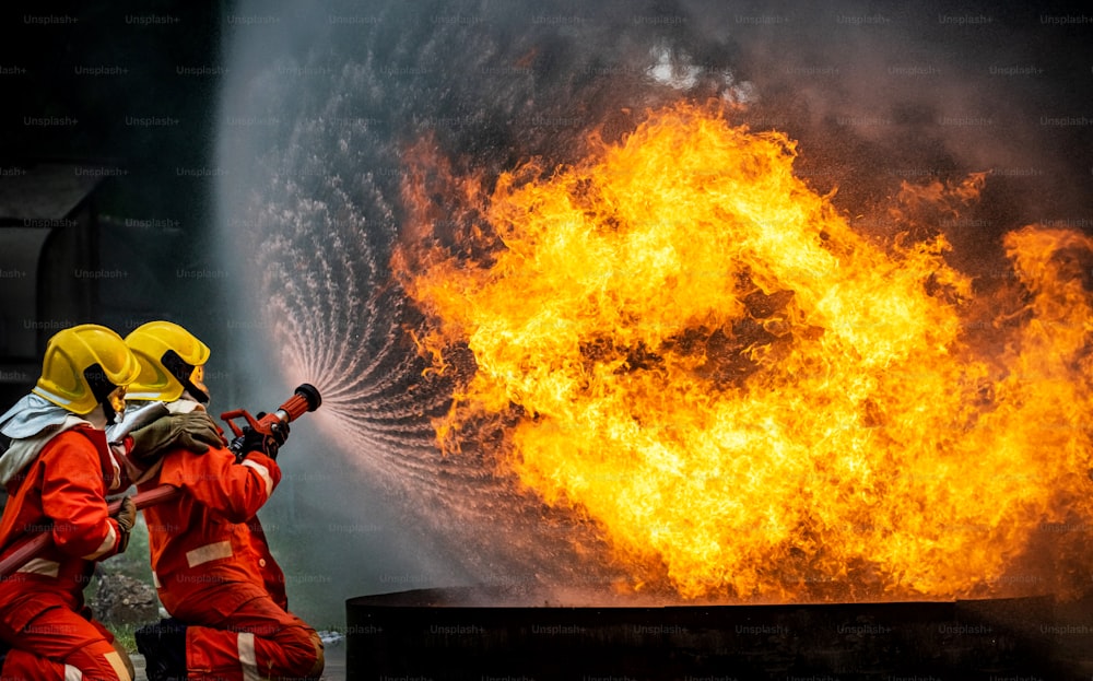 Two Firefighter teamwork in fire suit with fire fighting equipment using high pressure water fight a fire