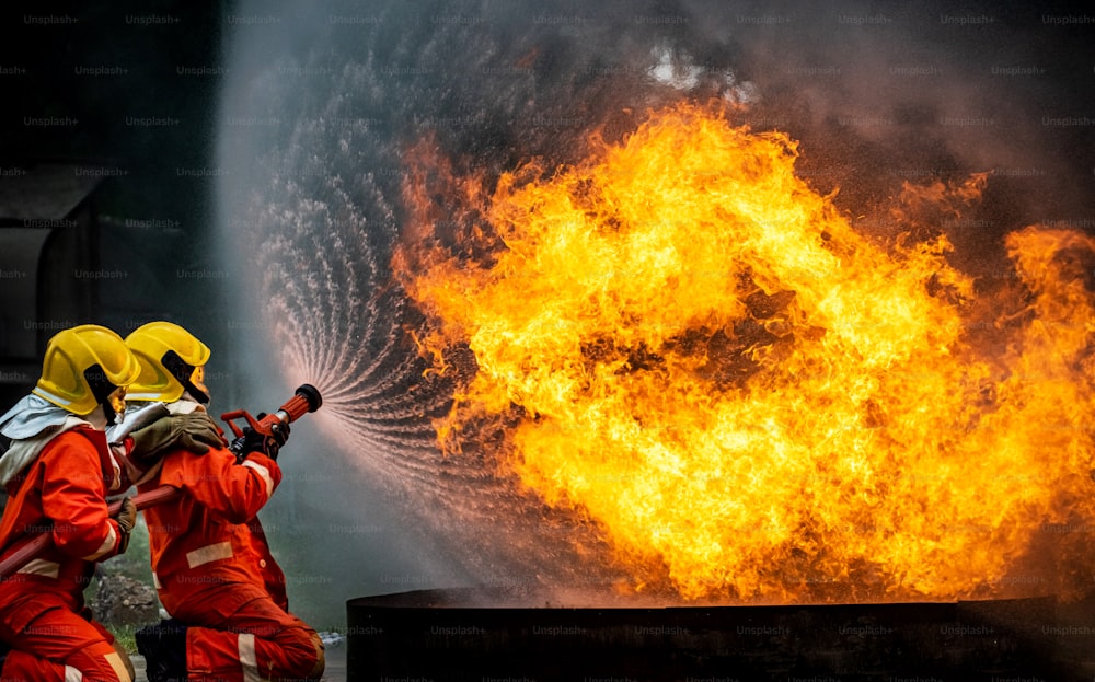 Dos equipos de bomberos trabajan en traje de bomberos con equipo de extinción de incendios que usa agua a alta presión para combatir un incendio