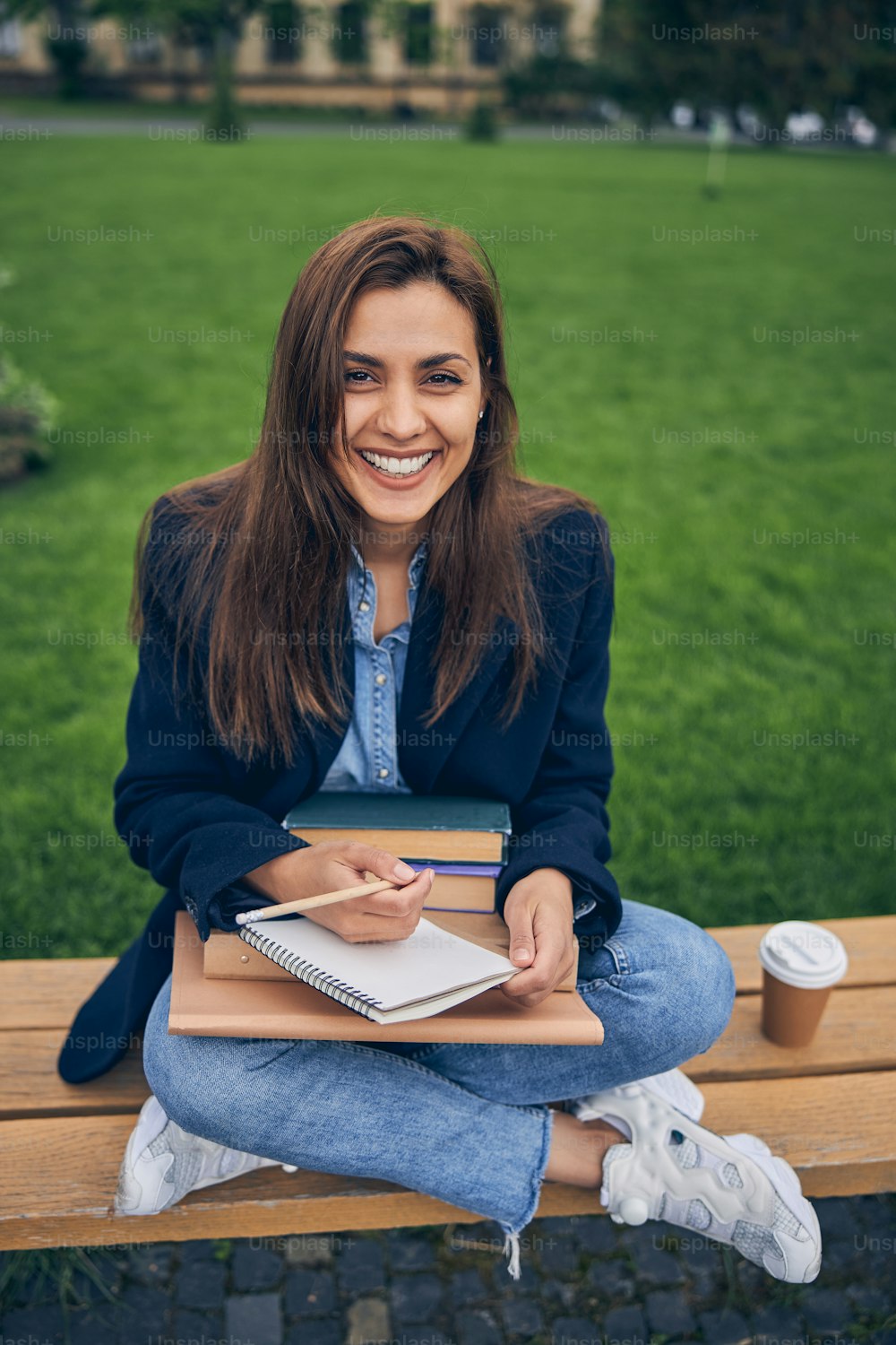 Beautiful smiling lady sitting on the bench with her legs while writing in notebook on her knees