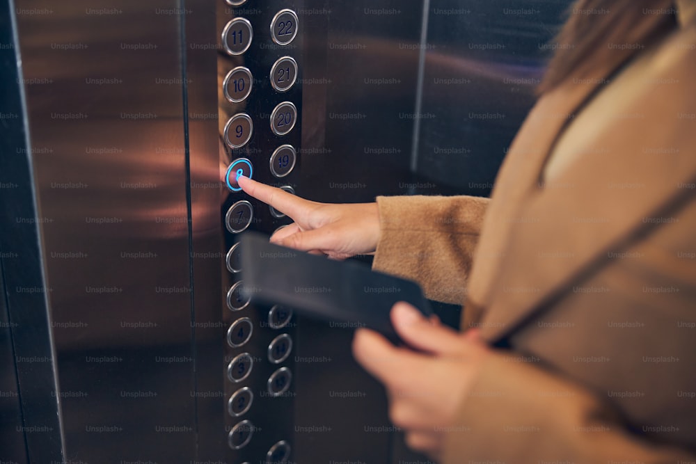 Close up photo of woman in brown coat pressing button of the lift to go down