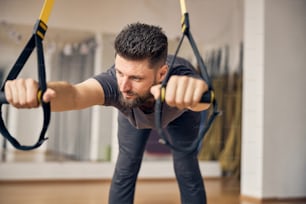 Hombre caucásico de pelo corto flexible de ensueño haciendo ejercicio de bisagra de cadera de postura ancha en un gimnasio