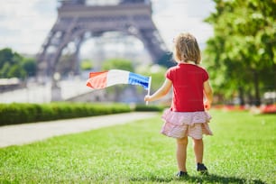 Menina bonita da criança com bandeira tricolor nacional francesa perto da torre Eiffel em Paris, França. 14 de julho (dia da Bastilha), principal feriado nacional francês