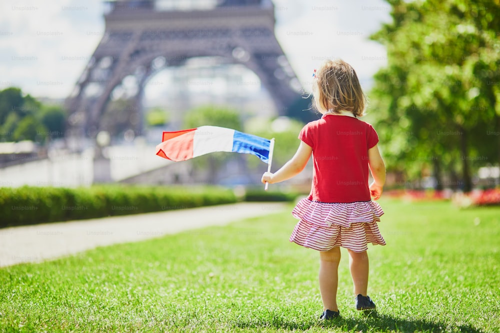 フランス、パリのエッフェル塔の近くにフランスの国の三色旗を持つ美しい幼児の女の子。7月14日(バスティーユの日)、フランスの祝日