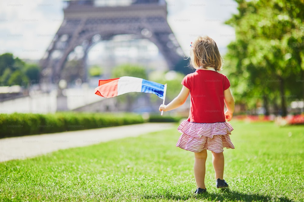 Beautiful toddler girl with French national tricolor flag near the Eiffel tower in Paris, France. 14 July (Bastille day), main French national holiday