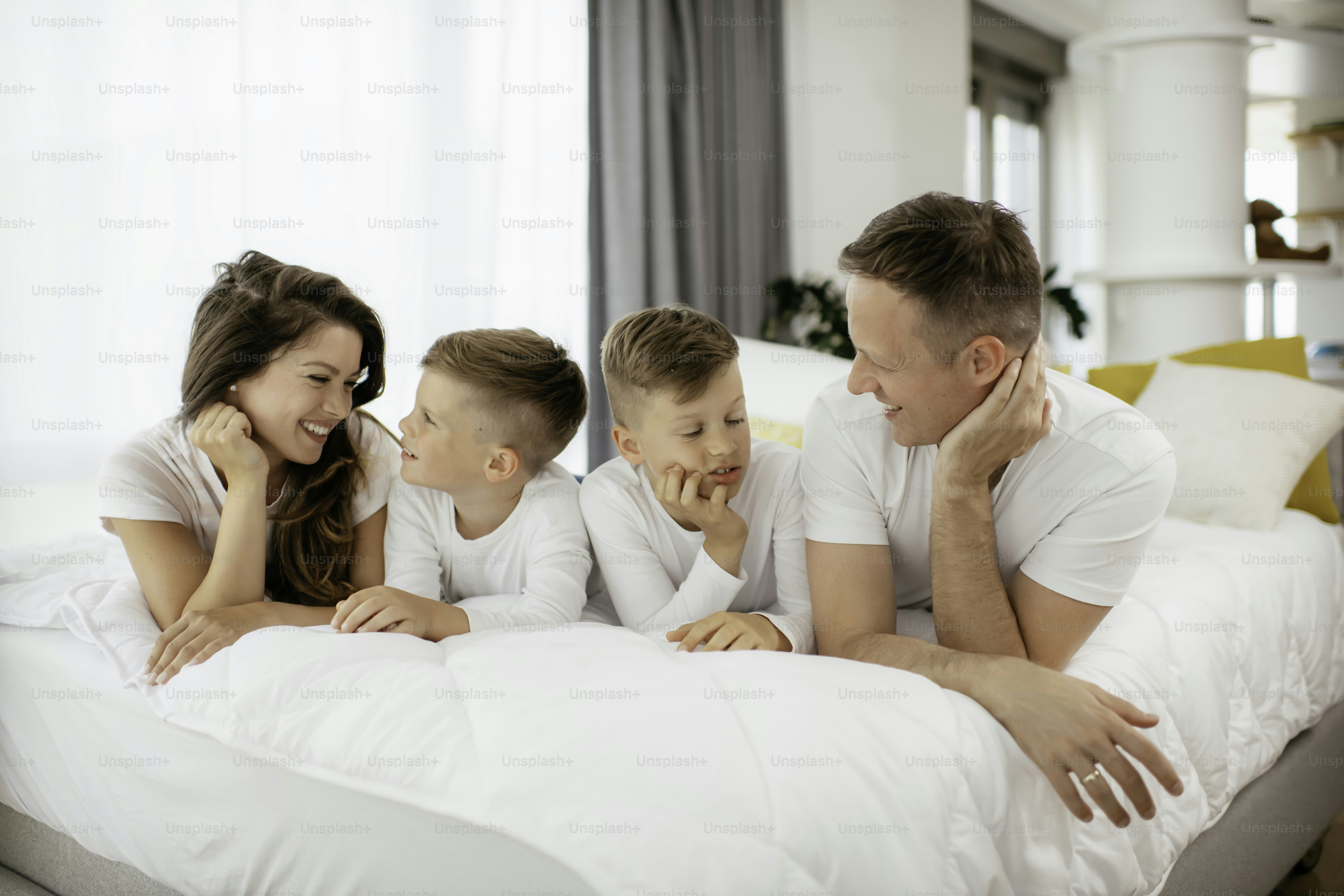 Young family enjoying at home. Happy parents with sons relaxing in bed.