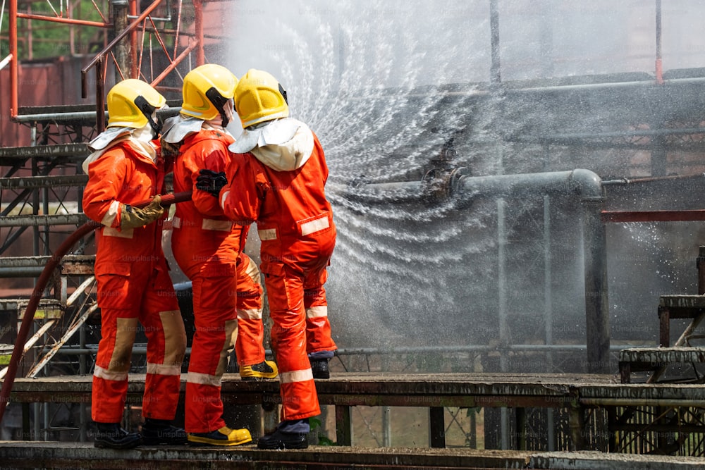 Grupo de Bombeiros em equipe em traje de incêndio com equipamentos de combate a incêndio utilizando água de alta pressão combate a incêndio