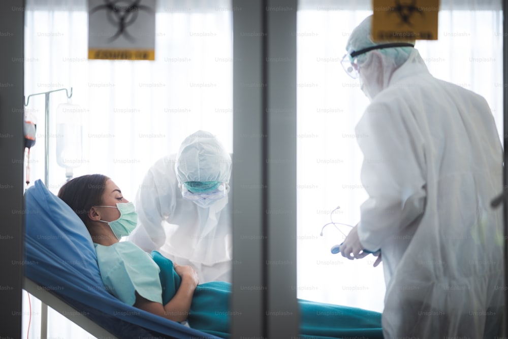 コロナウイルスの病気の治療のために働くウイルス制御の専門家の医師COVID-19に感染した患者、病院の検疫陰圧室の人々、PPEスーツの制服