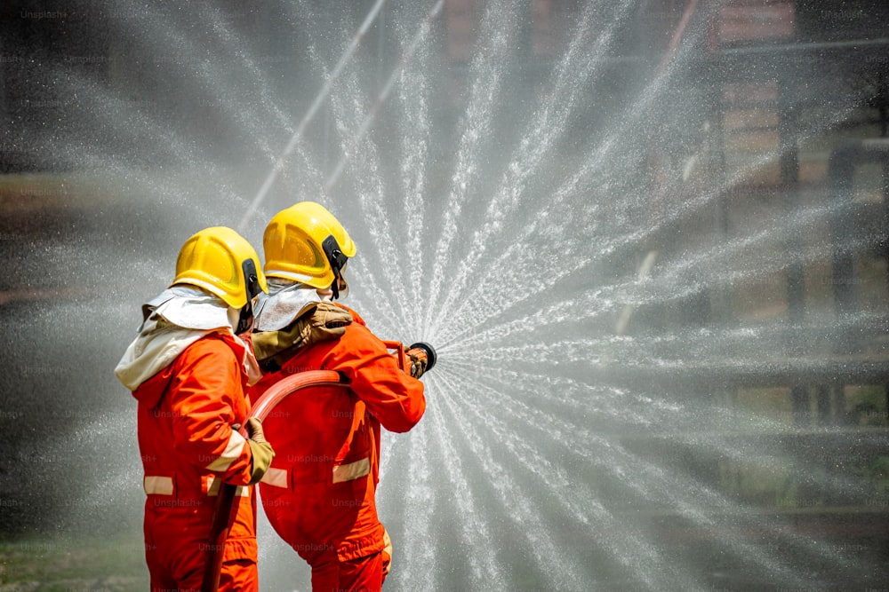 Dois bombeiros em equipe em traje de incêndio com equipamento de combate a incêndio usando água de alta pressão combater um incêndio