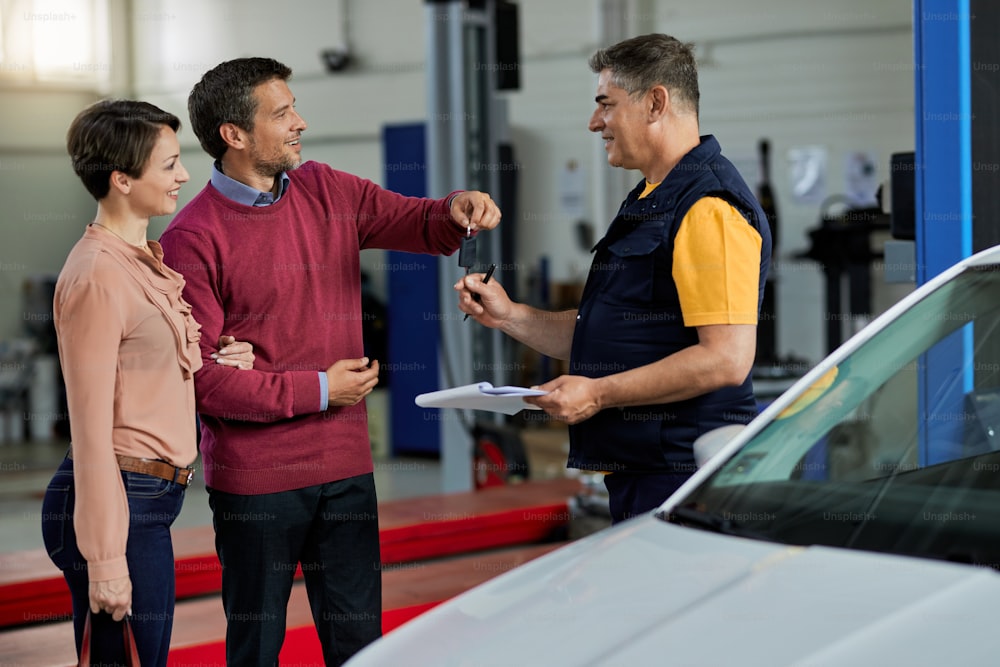 Happy couple handing over car key to their mechanic in auto repair shop.