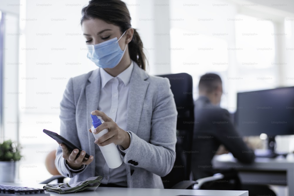Businesswoman disinfecting smart phone in office. Covid-19