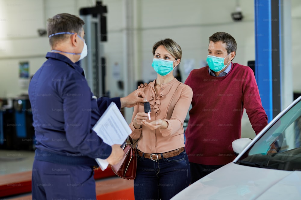 Satisfied customers receiving their car key from auto repairman in a workshop.