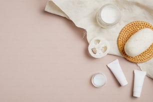 SPA natural organic cosmetics set with towel on beige background. Flat lay, top view moisturizer cream, homemade soap, cream tubes, loofah. Skin care concept.
